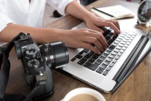 Hands typing on laptop next to camera – digital creator planning Onlyfans job application or side gig work