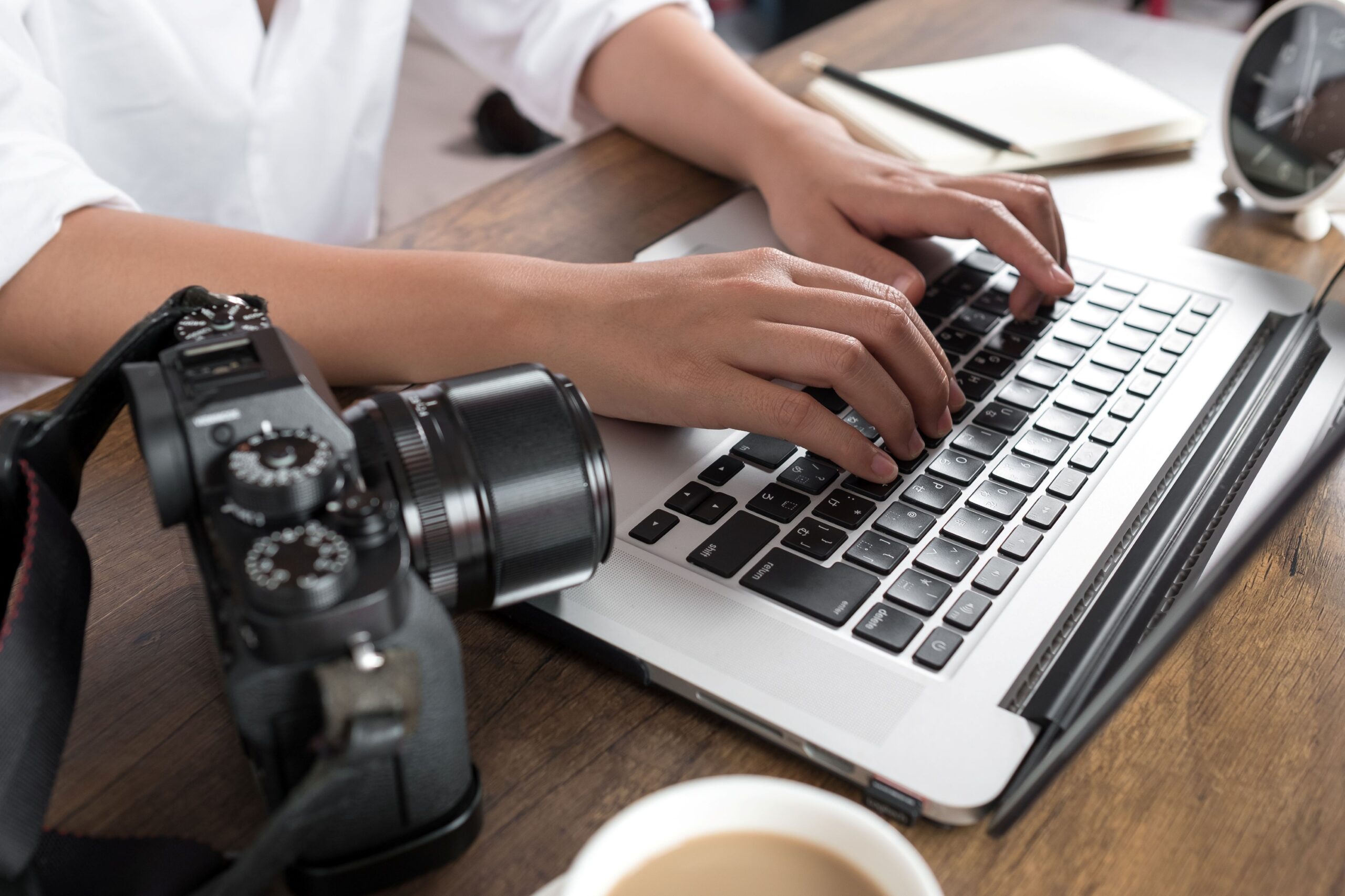 Hands typing on laptop next to camera – digital creator planning Onlyfans job application or side gig work
